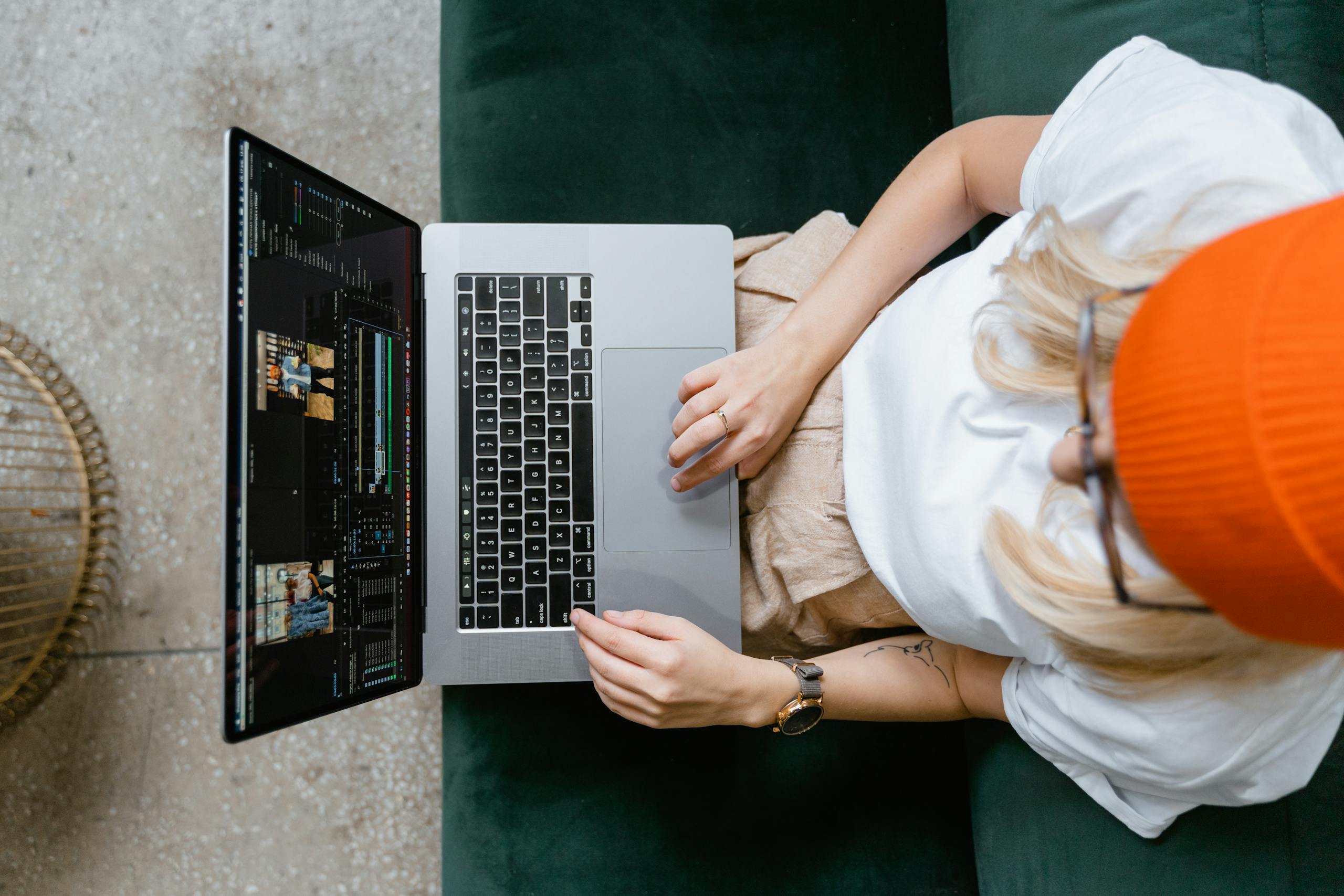 Top view of a woman editing video content on a laptop, wearing a casual outfit and orange beanie.